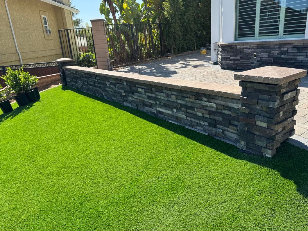 Modern backyard patio with stacked-stone retaining wall and bright green lawn
