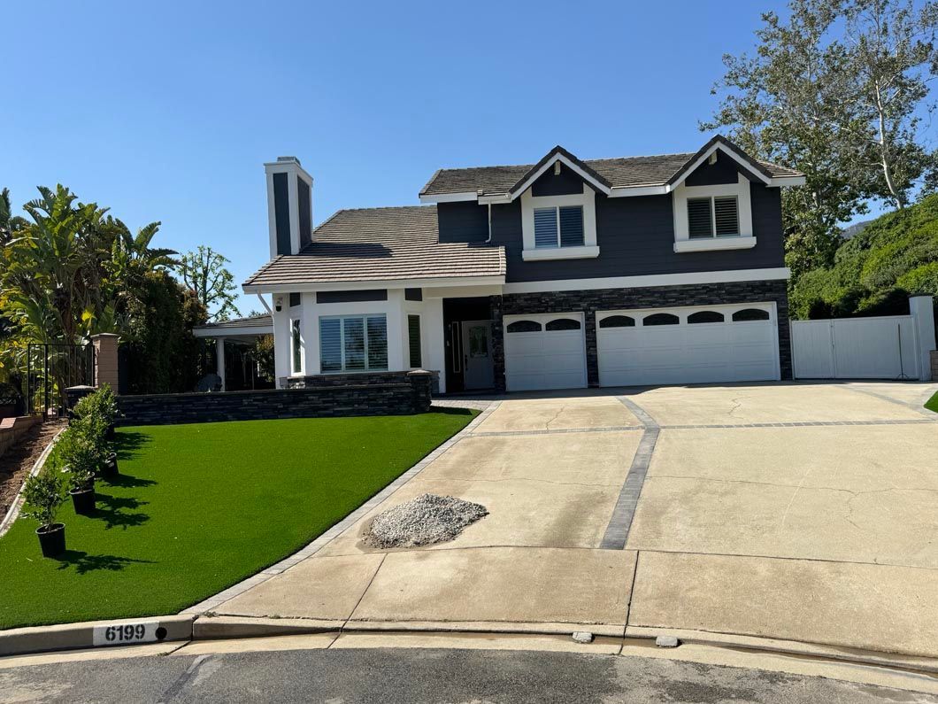 Two-story suburban house with white garage, dark roof, and sloped driveway beside a green lawn