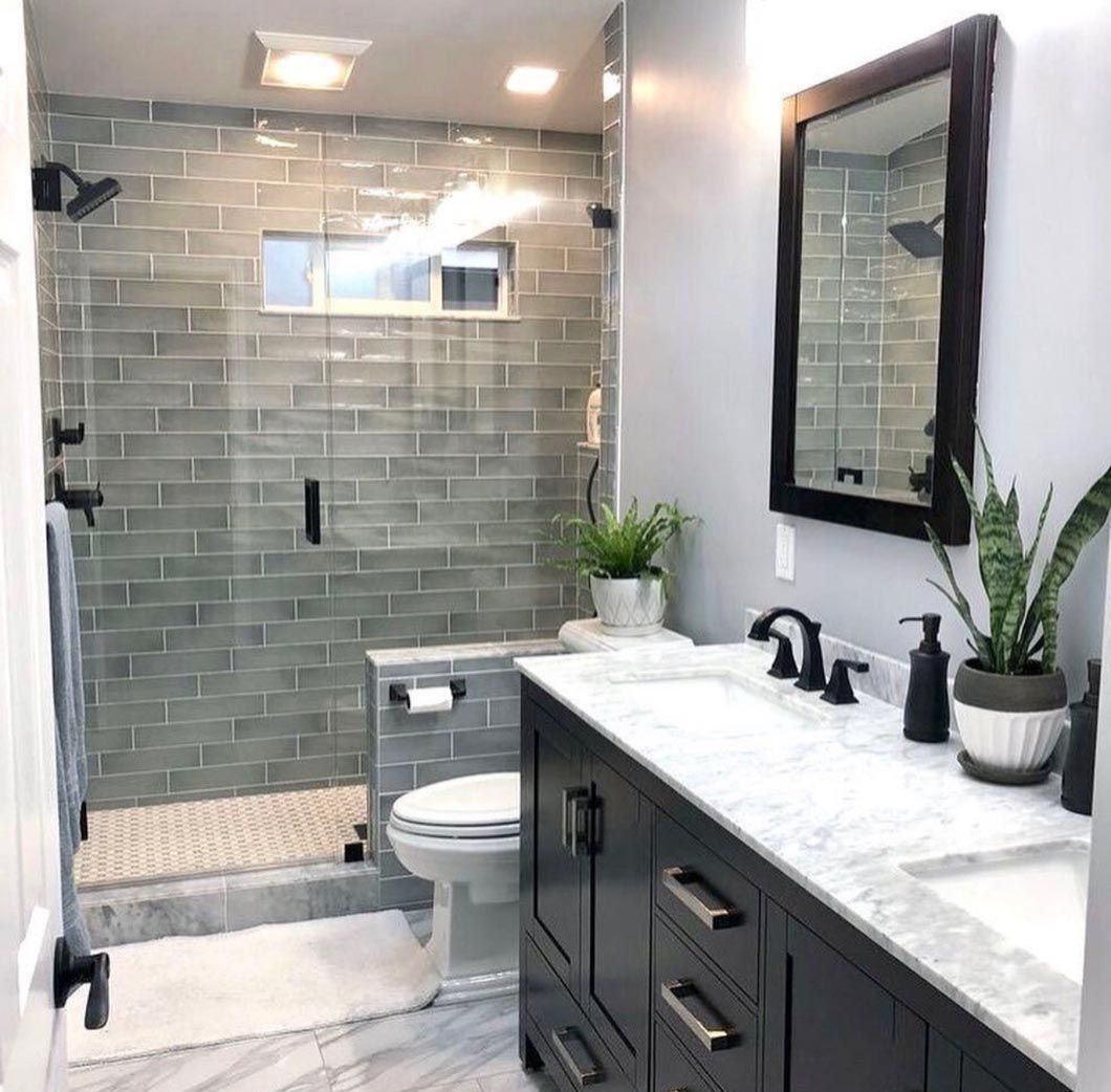 Modern bathroom with glass shower, gray tile, double vanity, and toilet beside a marble countertop