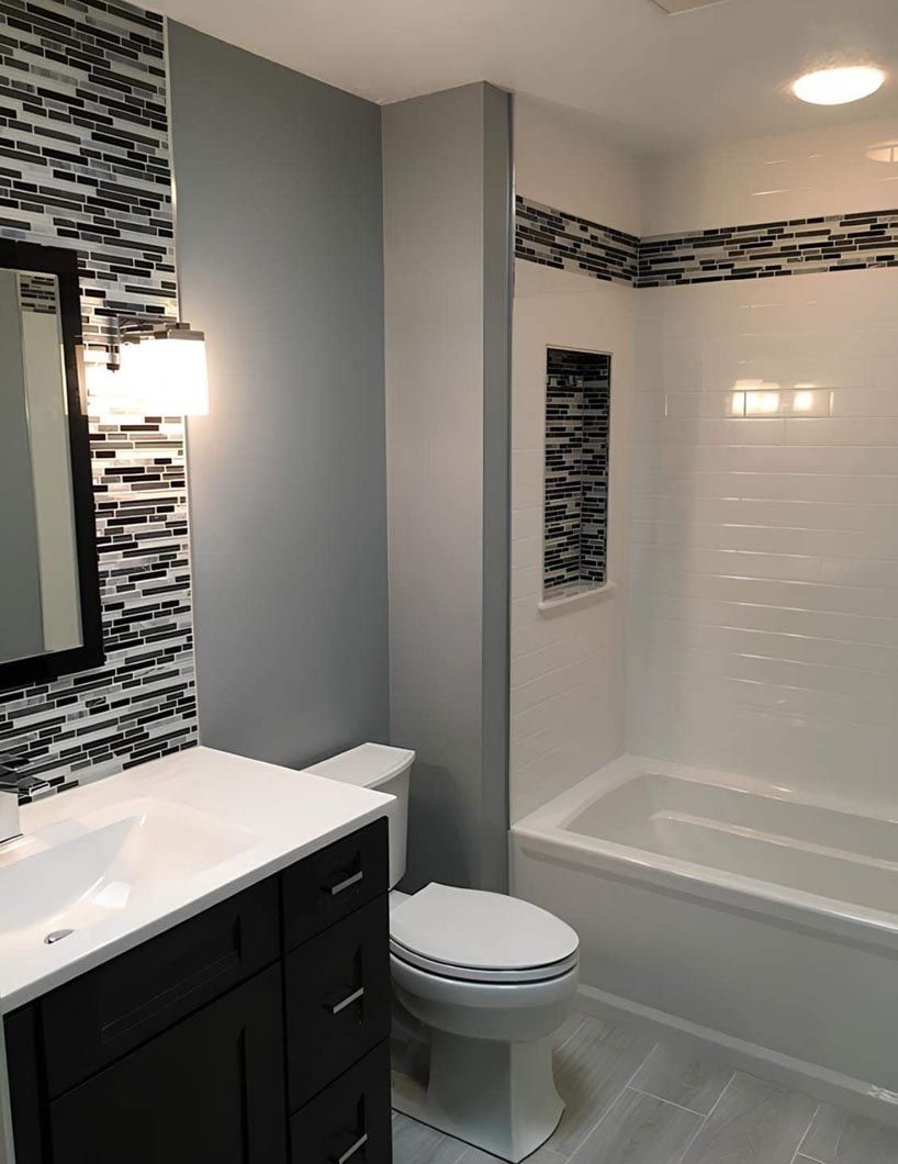Bathroom with black vanity, toilet, and white shower/tub surround, accented by dark mosaic tile.