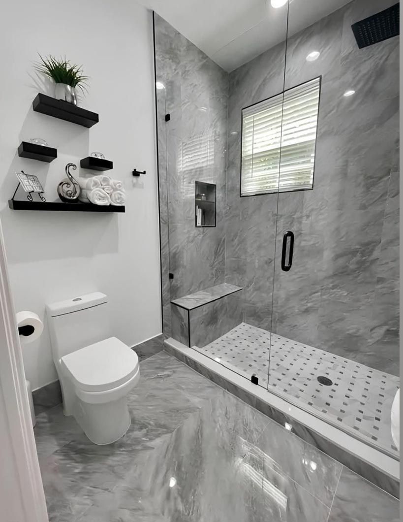 Modern gray-tile bathroom with walk-in shower, toilet, window, and black shelving.