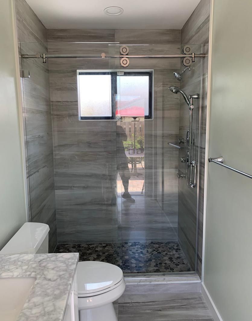 Small modern bathroom with gray tile shower, window, toilet, and marble vanity.