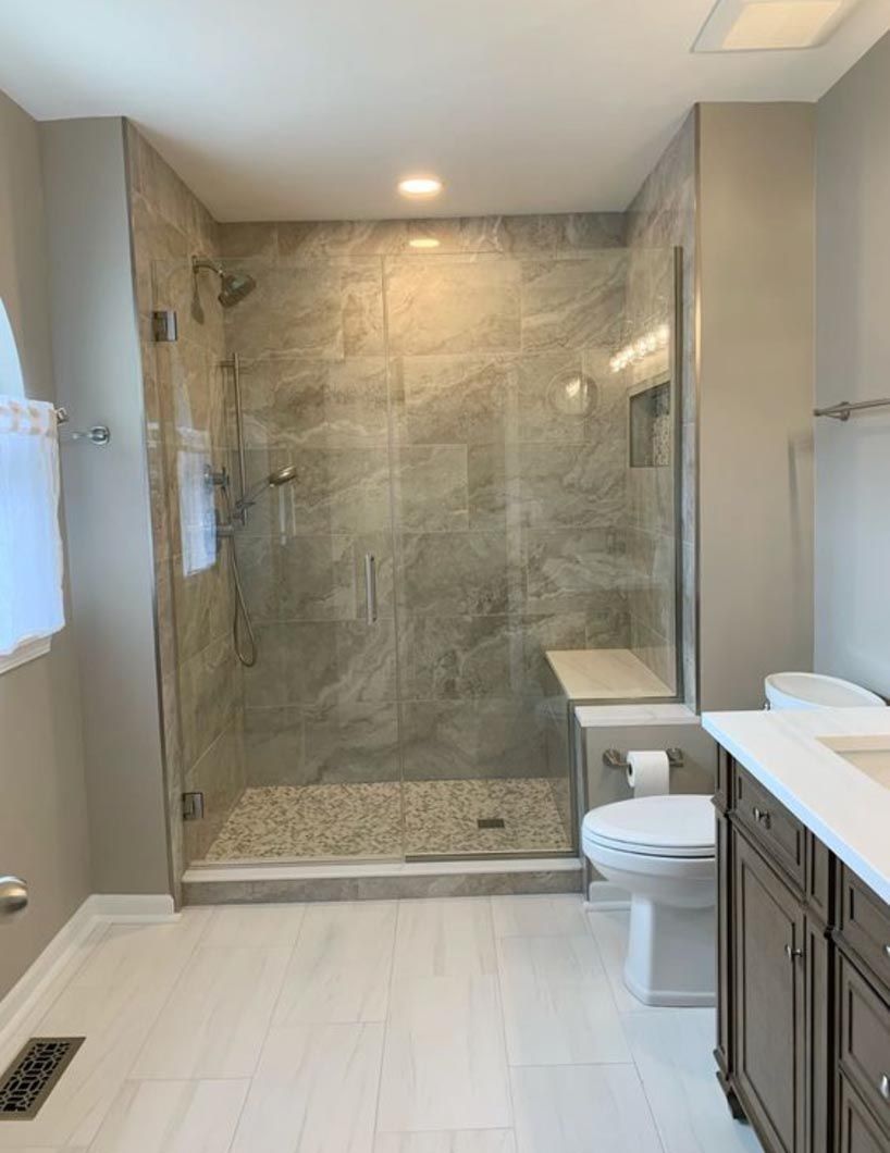 Modern bathroom with glass shower, white tile floor, and dark vanity with sink and toilet