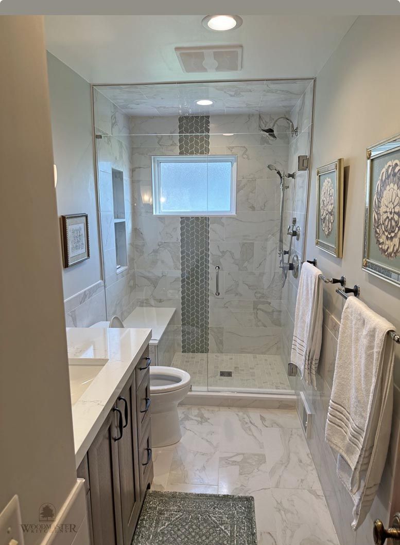 Modern bathroom with glass shower, marble tile, vanity, and towels hanging on the wall
