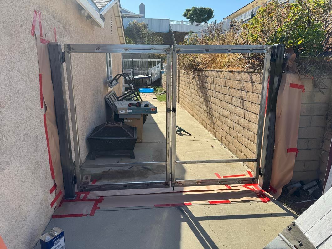 Narrow outdoor passage with a metal gate, brick wall, and red markings on the ground.