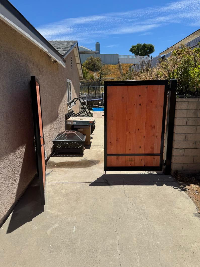 Narrow concrete courtyard with open wooden gate, stucco walls, and a blue sky in the background