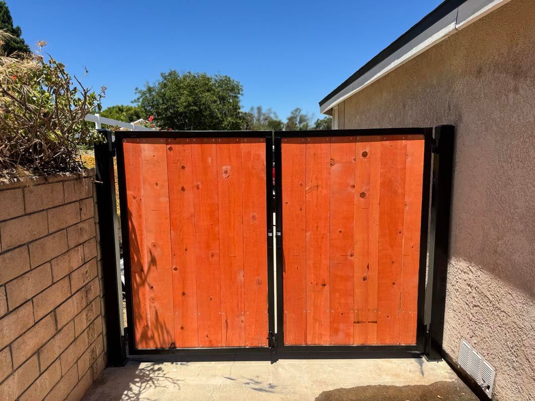 Orange double gate with black frame between a brick wall and a stucco house under a blue sky