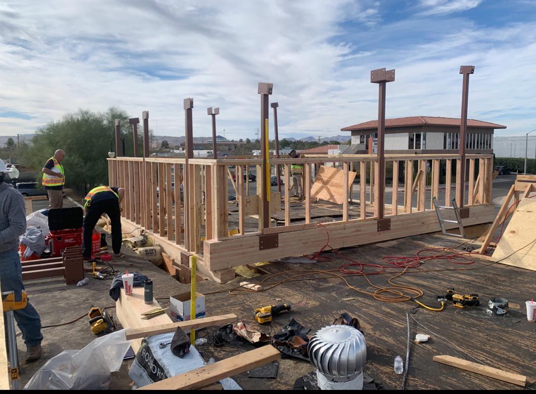 Construction crew framing a wooden house foundation on a muddy site under a cloudy sky