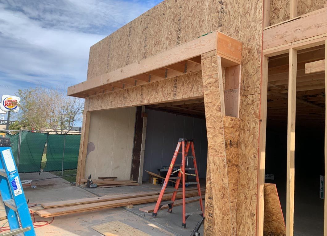 Construction site with unfinished building entrance, orange ladder, and exposed wood framing.