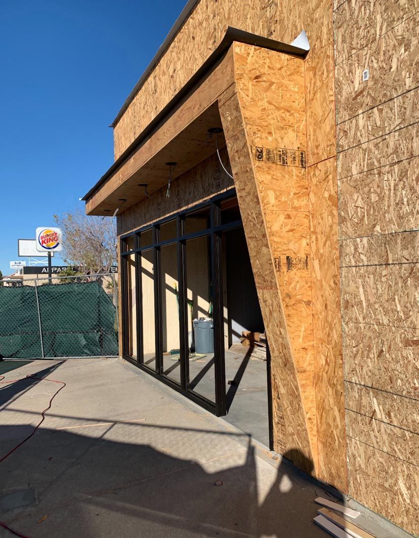Partially built storefront with OSB siding and large glass windows along a sidewalk