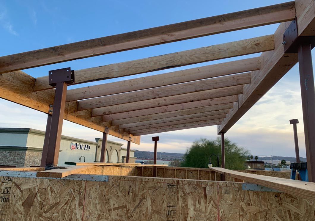 Wooden pergola frame over a construction site with exposed insulation and a sunset sky in the background