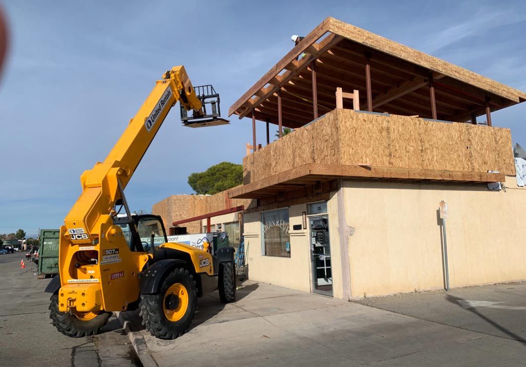 Yellow telescopic forklift lifting materials beside a building under construction