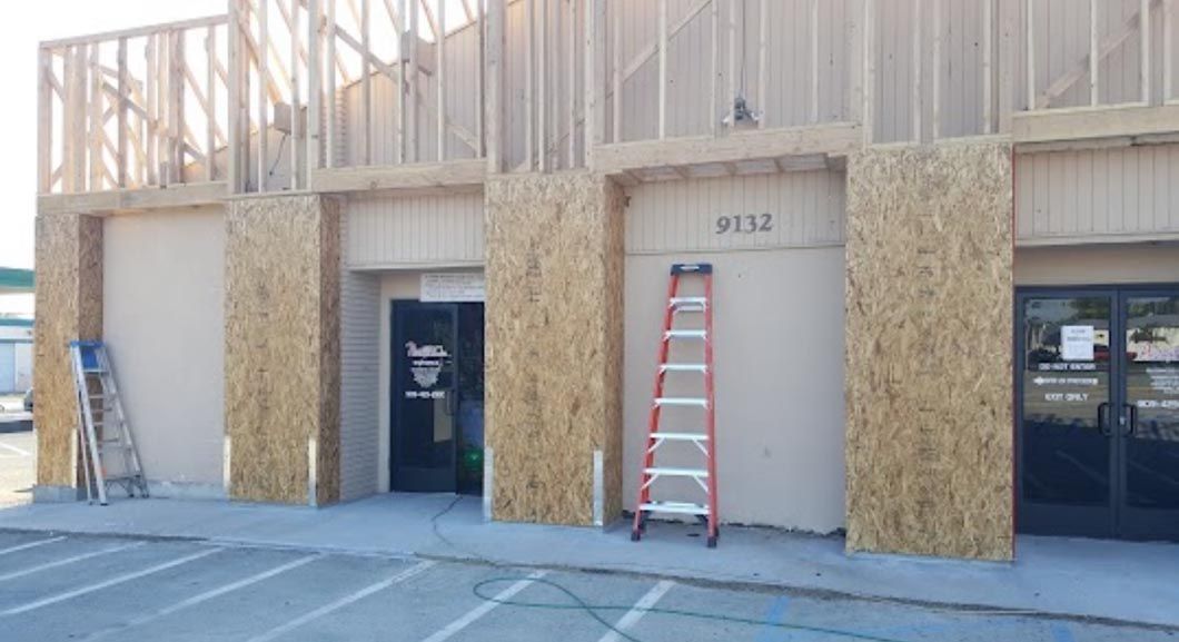 Building facade under construction with plywood walls, two ladders, and a roll-up door numbered 3132.
