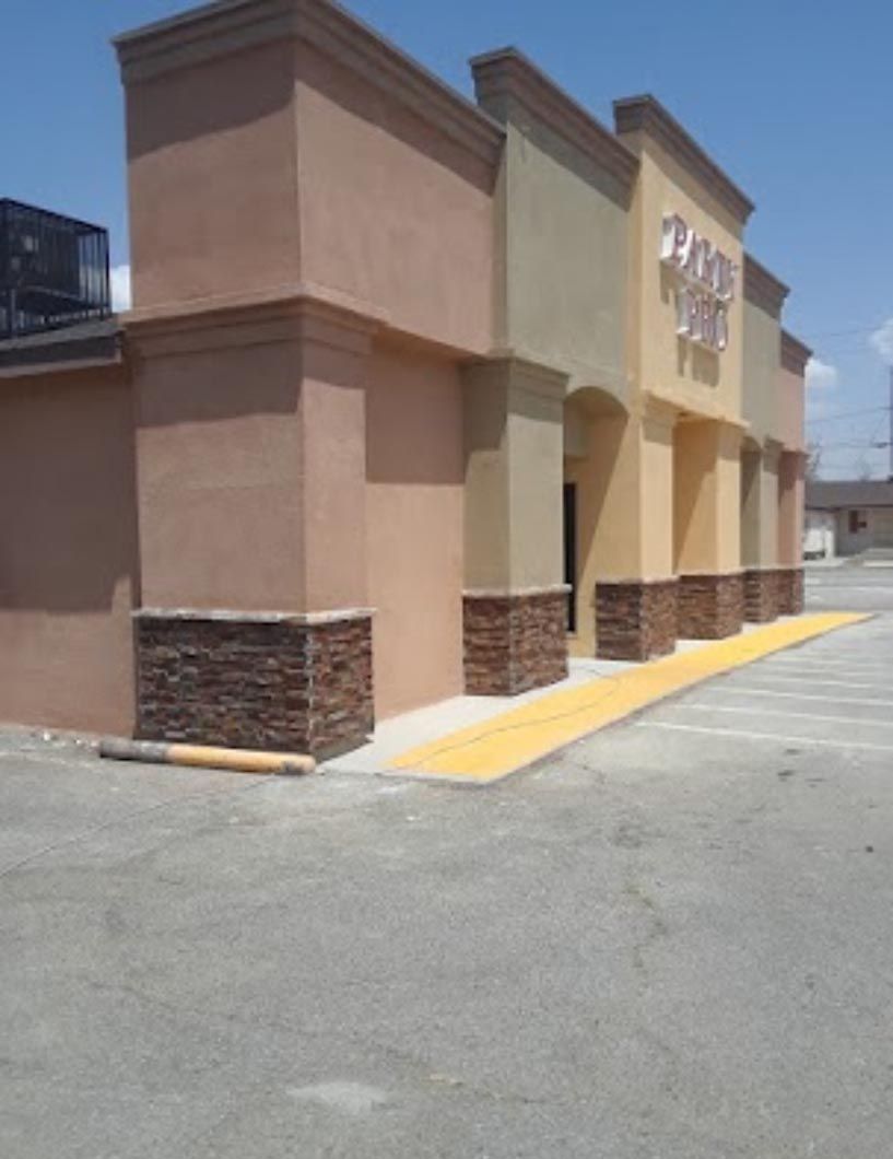Storefront with tan walls, stone trim, and a yellow accessibility ramp along a parking lot