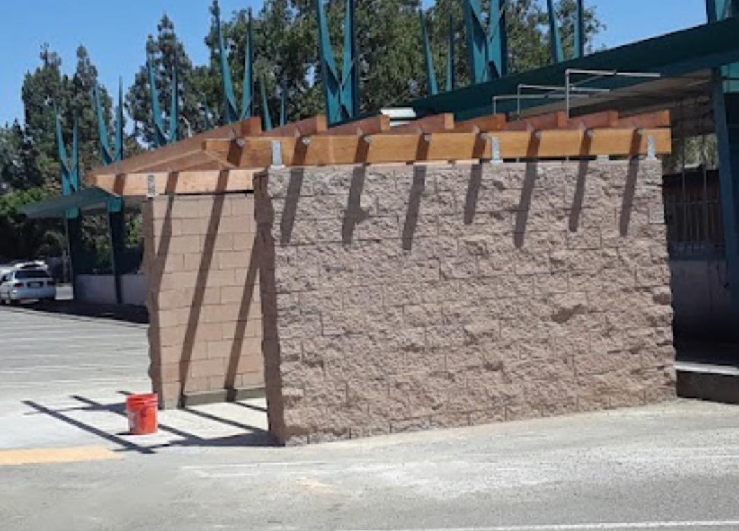 Large tan wall with wooden supports and blue flags outdoors on a sunny street corner