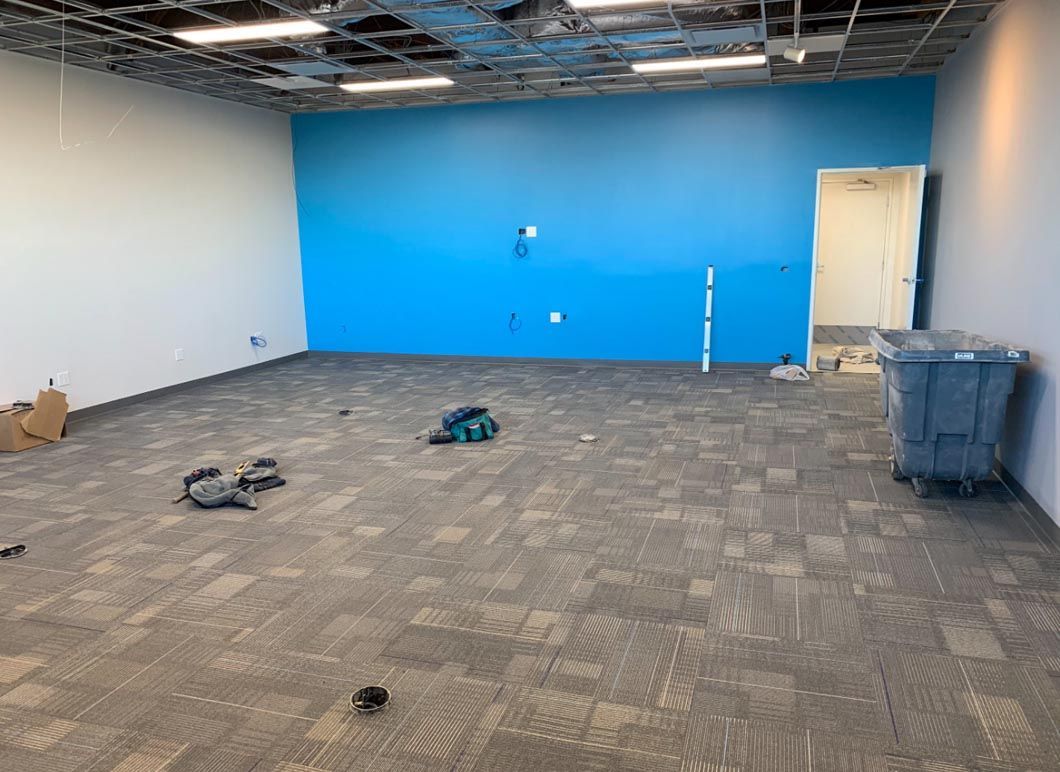Empty office under renovation with blue accent wall, exposed ceiling, and carpet tiles on the floor