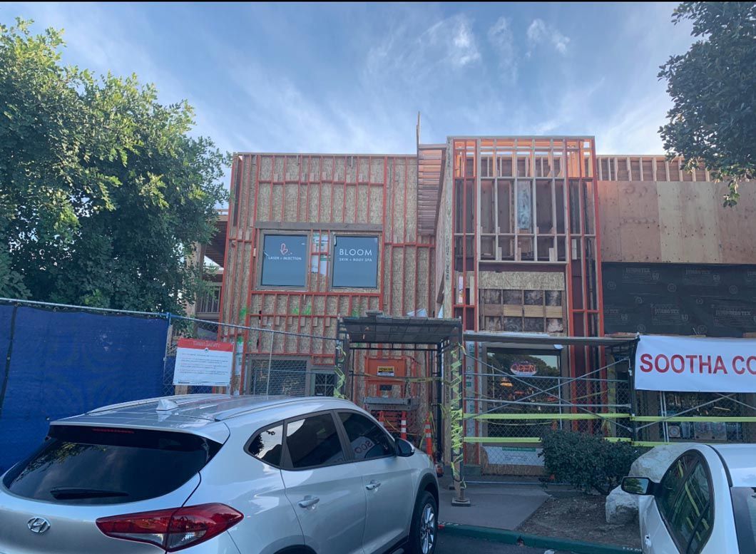 Street view of a construction-site building with scaffolding, trees, and parked cars in front