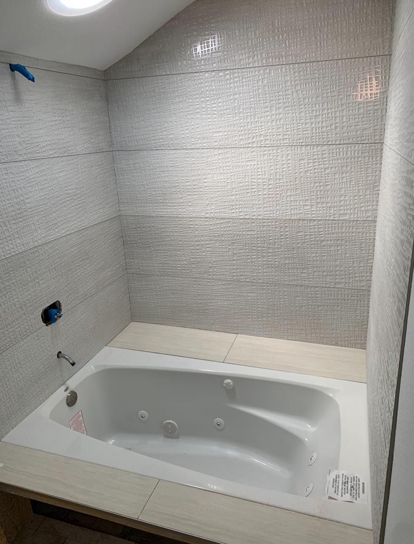 Bathroom with a white soaking tub against textured gray tile walls.