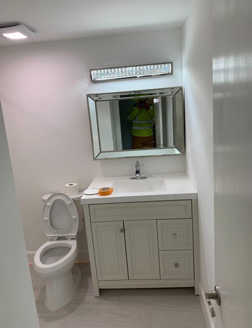 Small white bathroom with toilet, vanity sink, mirror, and frosted window.