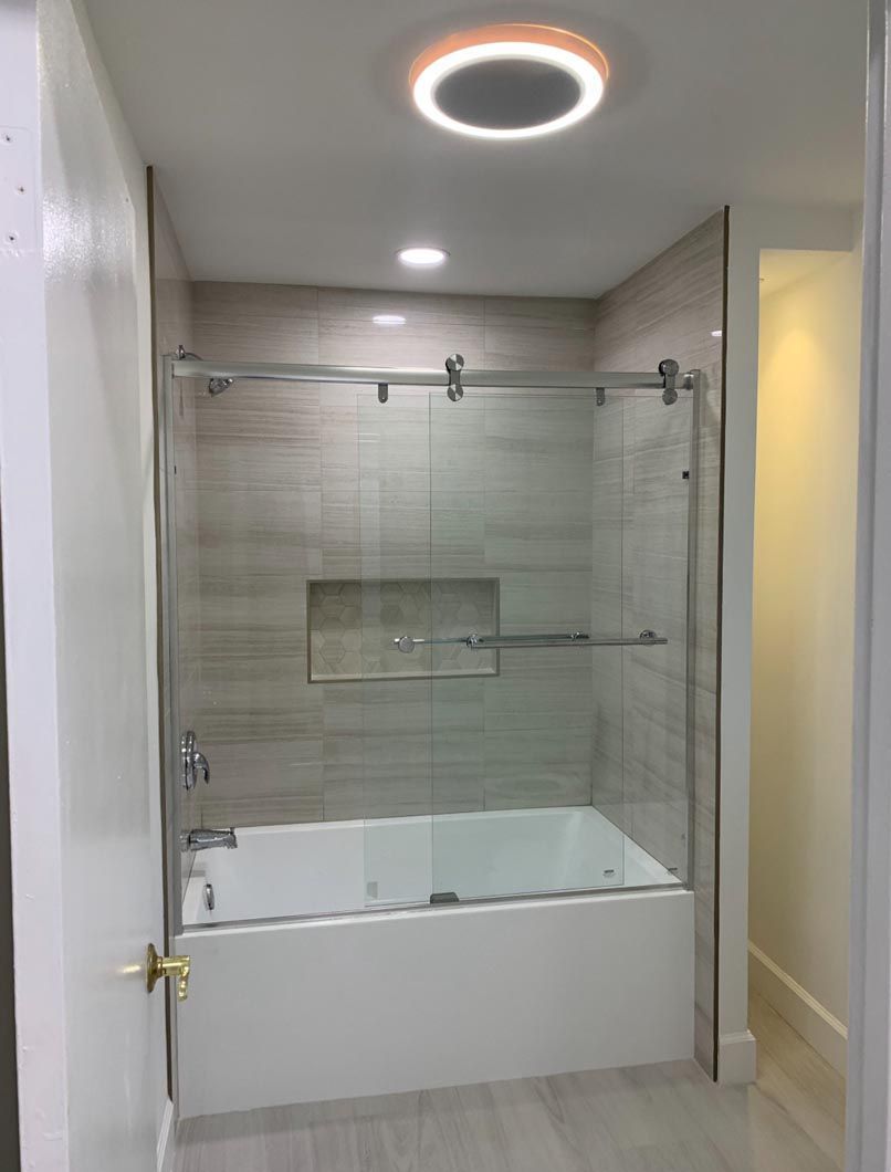 Modern bathroom with bathtub, glass shower door, tiled wall, and circular ceiling light