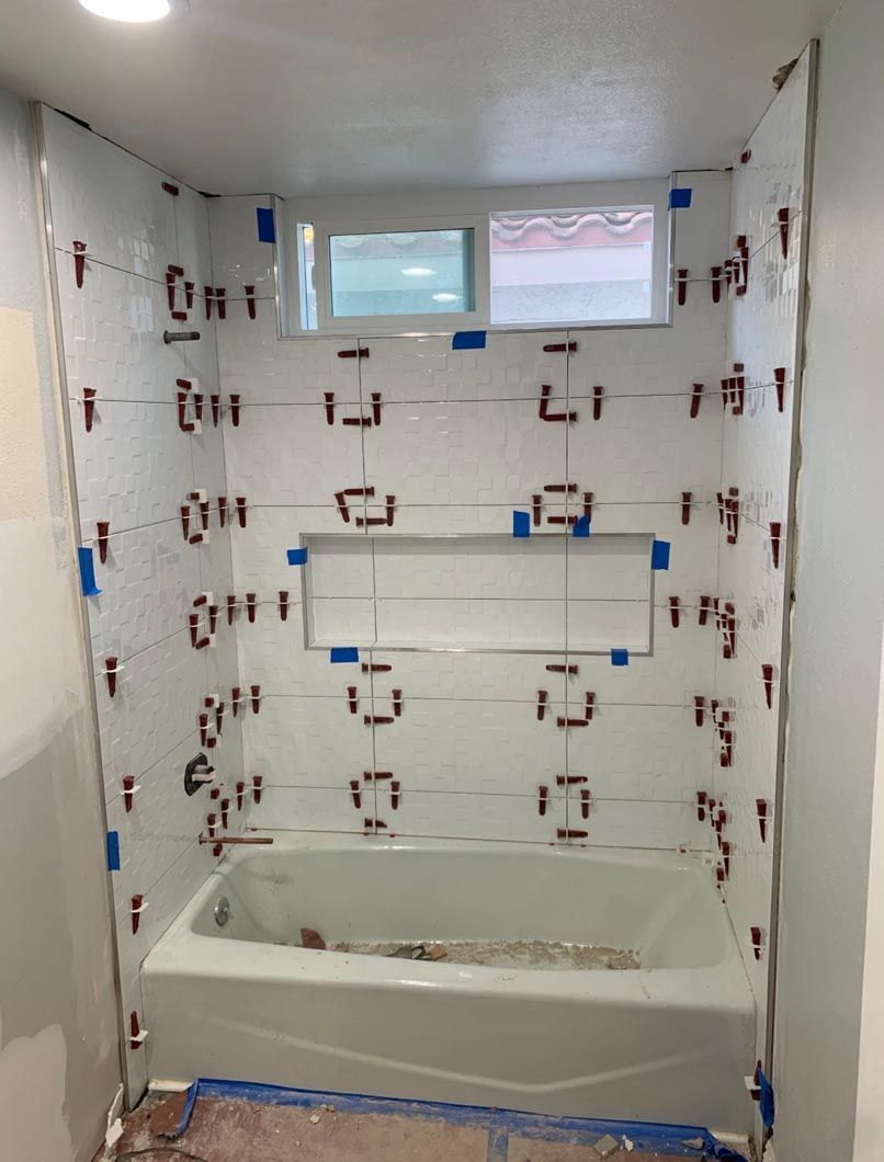 Bathroom shower/tub alcove with white tile, window, and masking tape marking wall spots for renovation.