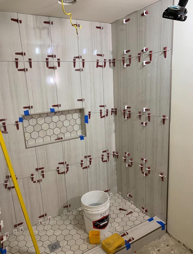 Tiled shower under construction with hanging clips, a paint bucket, and tools on the floor.