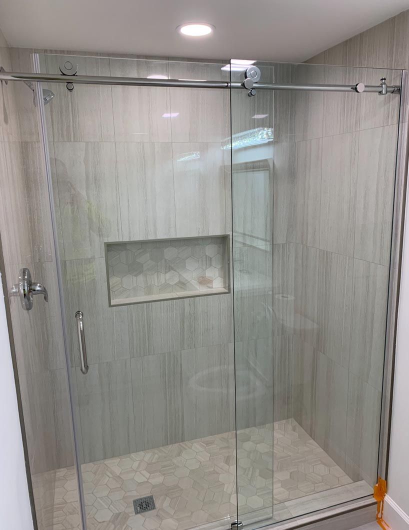 Glass-enclosed shower with gray tile walls, built-in niche, and light stone floor.