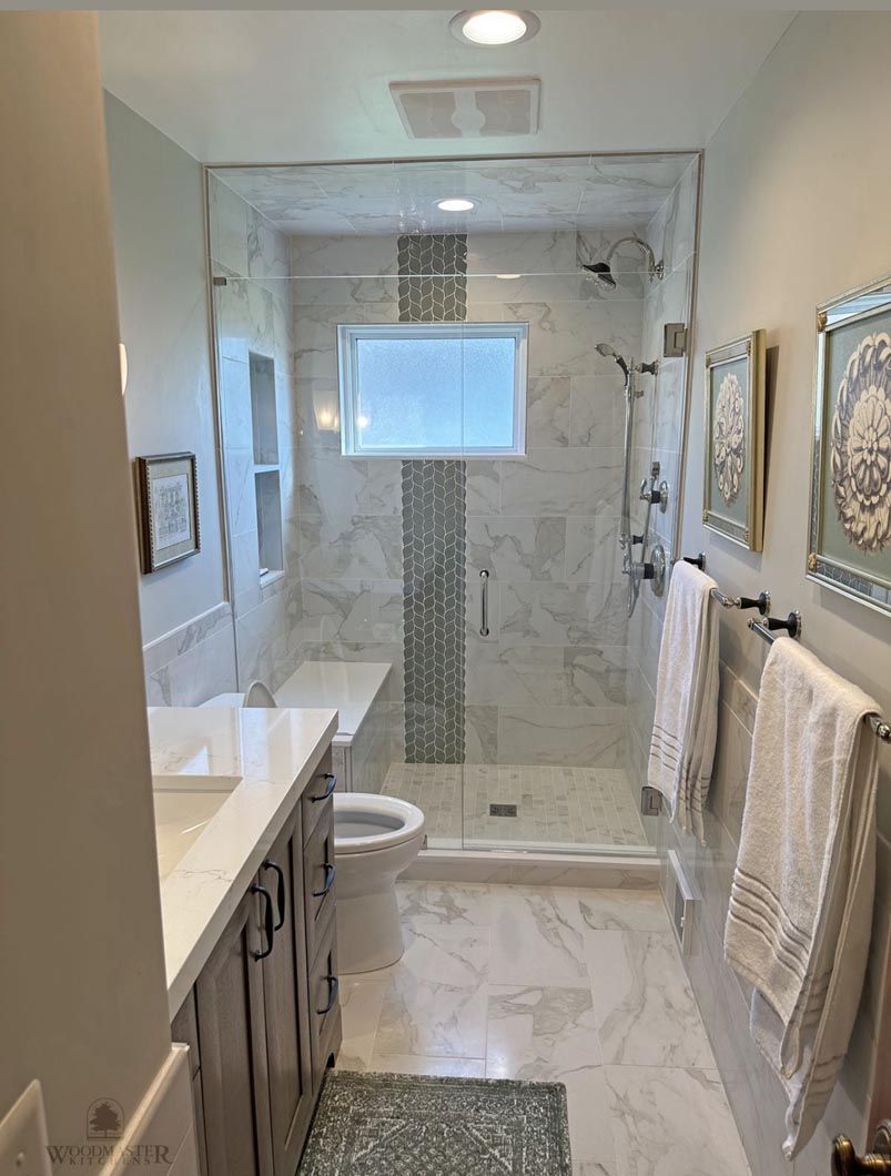 Narrow marble bathroom with glass shower, vanity, and wall towels, in white and gray tones