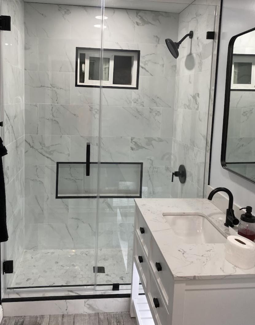 Modern bathroom with glass shower, white marble walls, and white vanity with black fixtures.