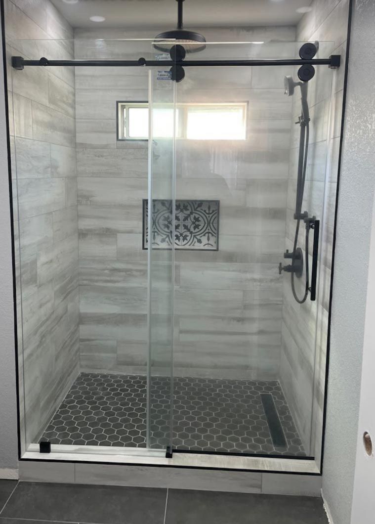 Modern glass shower enclosure with gray tile walls, black fixtures, and pebble floor accents