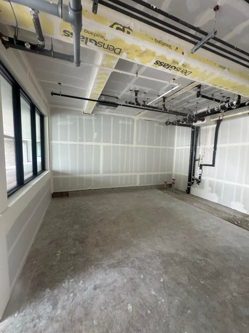 Empty unfinished room with drywall, concrete floor, exposed ceiling framing, and large windows