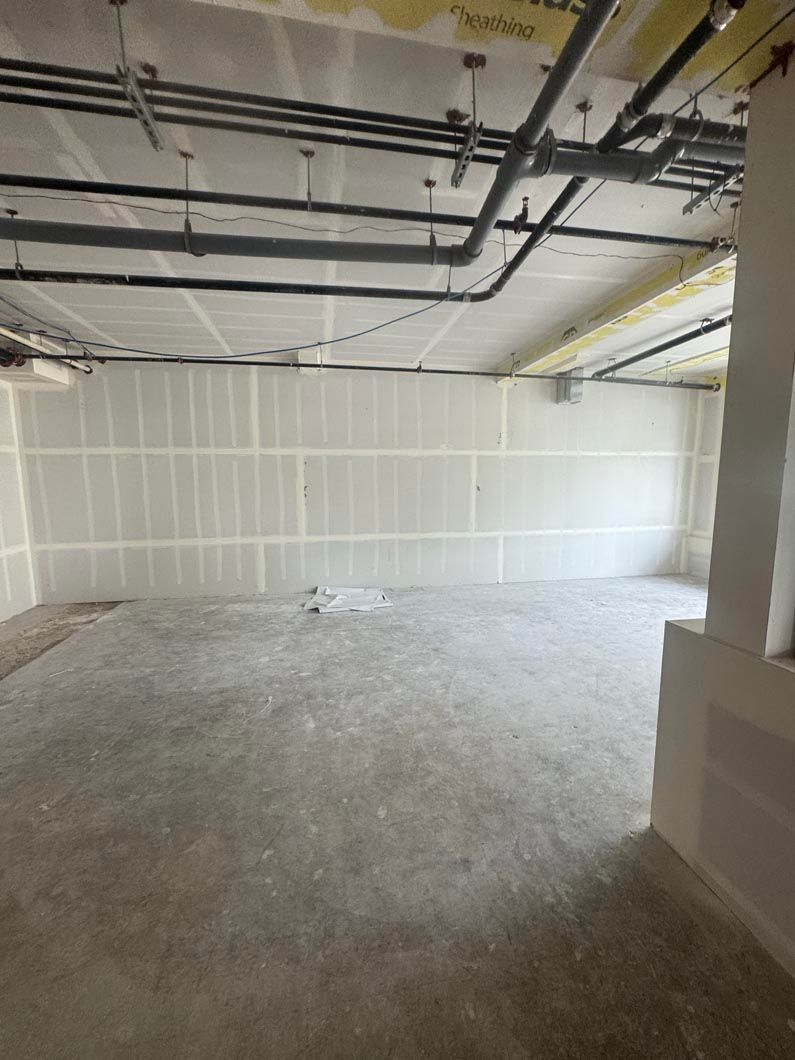 Empty unfinished room with exposed ceiling pipes, white walls, and concrete floor