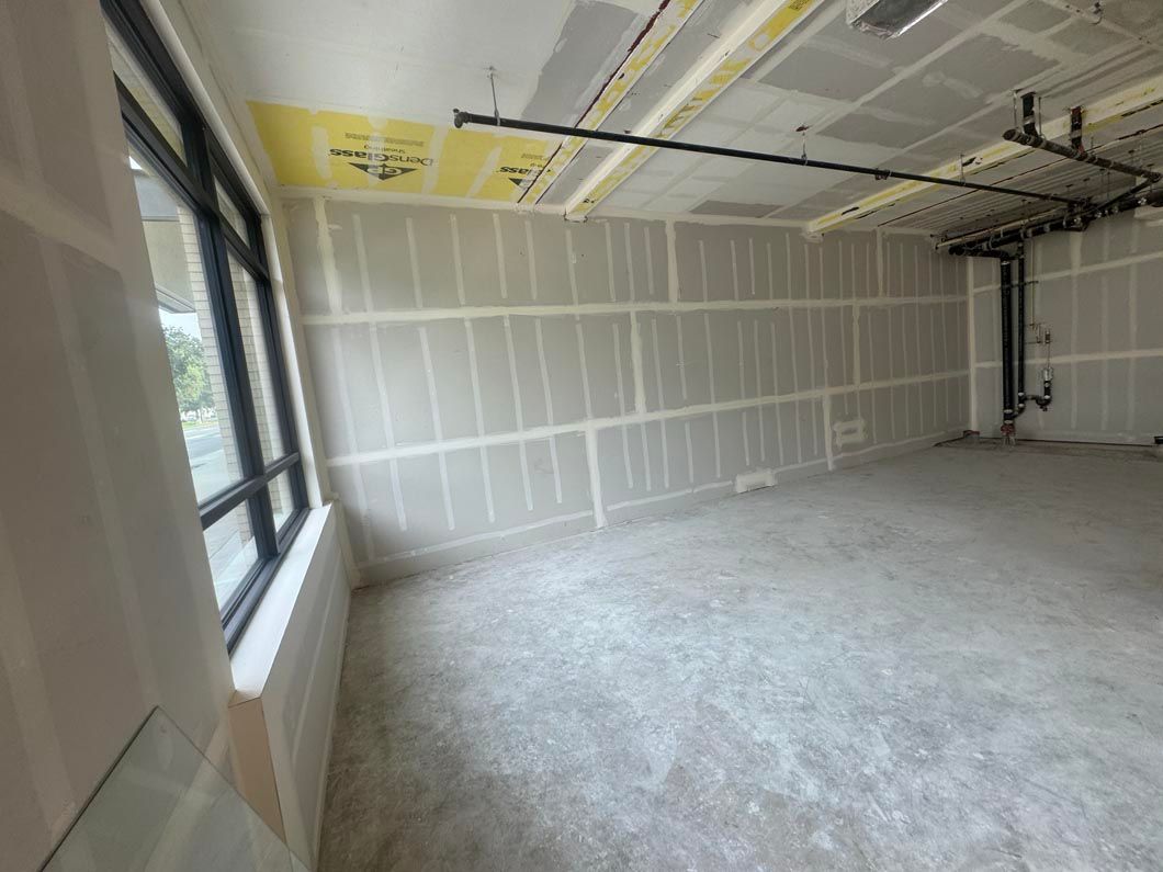 Empty unfinished room with drywall, concrete floor, and large windows on the left