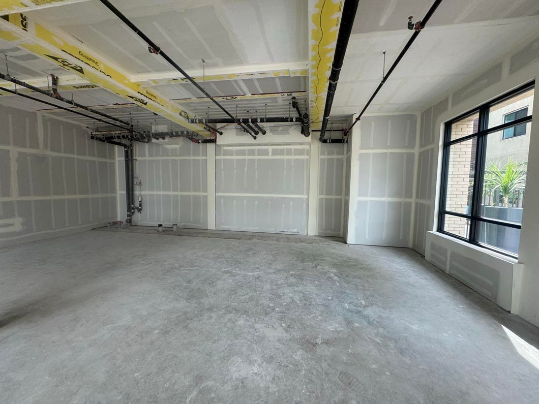 Empty unfinished room with drywall, exposed ceiling ducts, and a large window on the right.