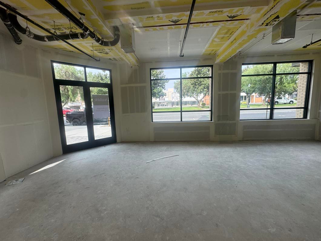 Empty unfinished room with exposed ceiling, white walls, and large windows and glass door facing outside