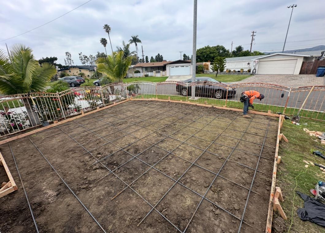 Concrete foundation being poured in a backyard, with workers and rebar framework visible.