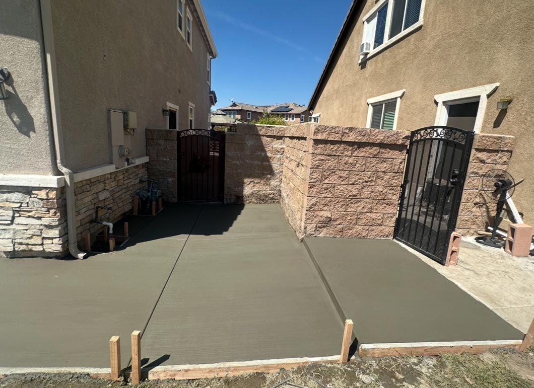 Fresh concrete patio between two stucco houses with stone walls and a black gate