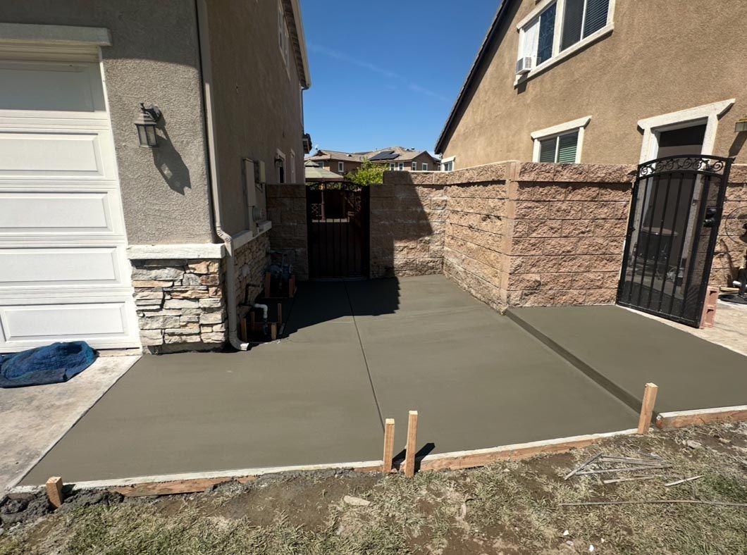 Freshly poured concrete driveway beside a house, with a brick wall and gate leading to a side yard