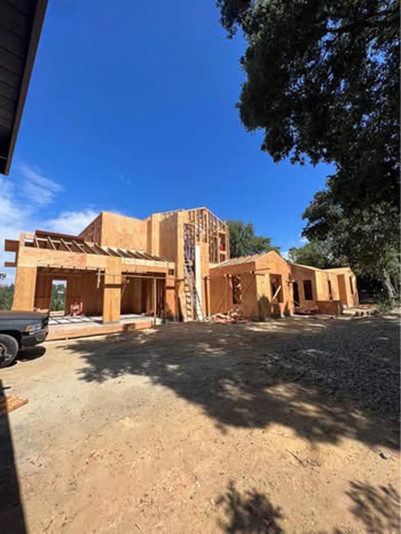 Sunlit unfinished brick house with open garage and dirt driveway under a blue sky