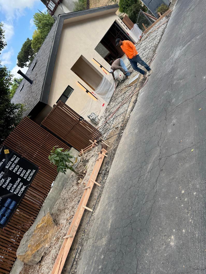 Person in orange shirt near a small house and fence on a slanted street.