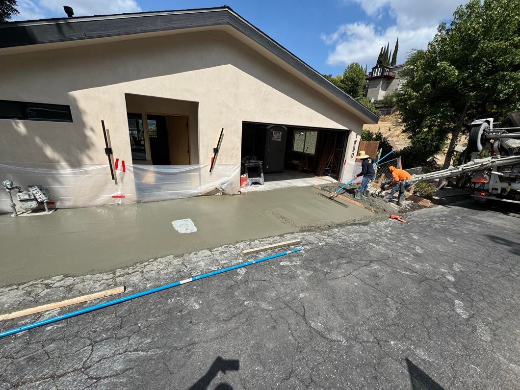 Partially demolished house exterior with exposed framing, debris, and a wet driveway under construction.