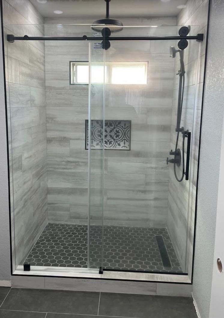 Glass shower enclosure with black hardware, patterned tile floor, and a small window above the tile accent.