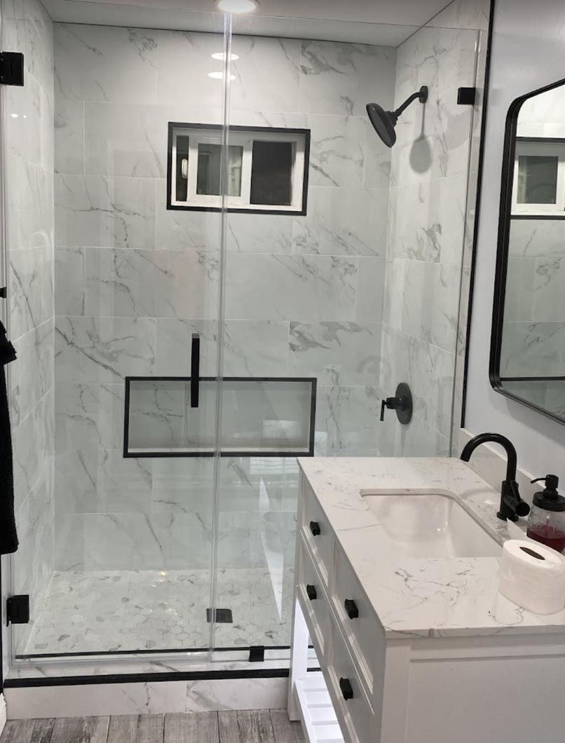 Modern bathroom with glass shower, white vanity, and black fixtures, shown in a bright marble-tiled space