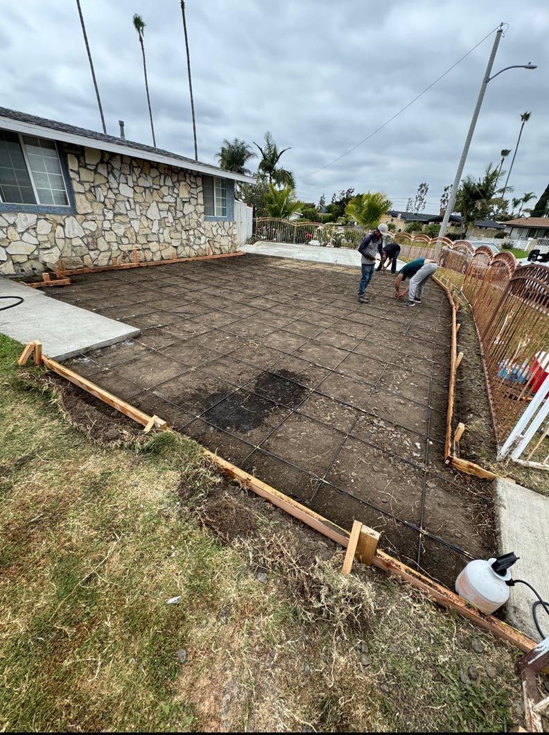 Construction site with rebar foundation, two workers, and a stone house under construction