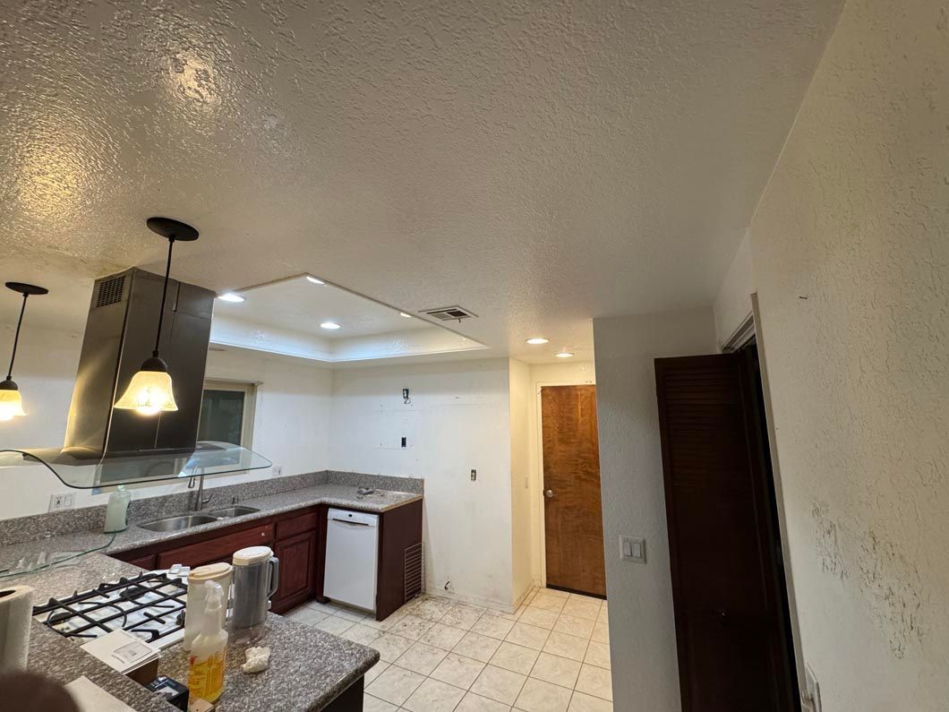 Open kitchen with white tile floor, dark cabinets, pendant lights, and a small dining area