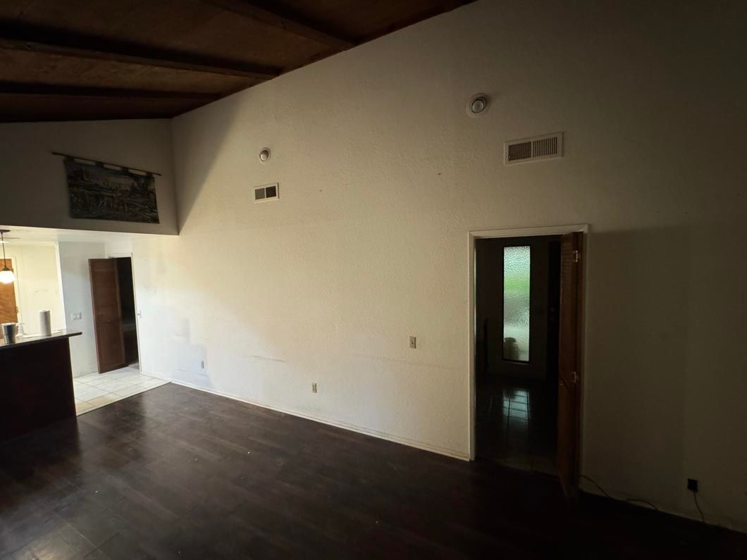 Empty room with dark wood floors, white walls, and two doorways, lit by daylight from the left.