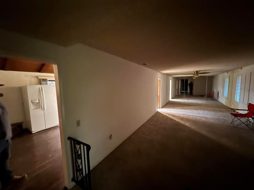 Long indoor hallway with white walls, dim lighting, and a doorway on the left.