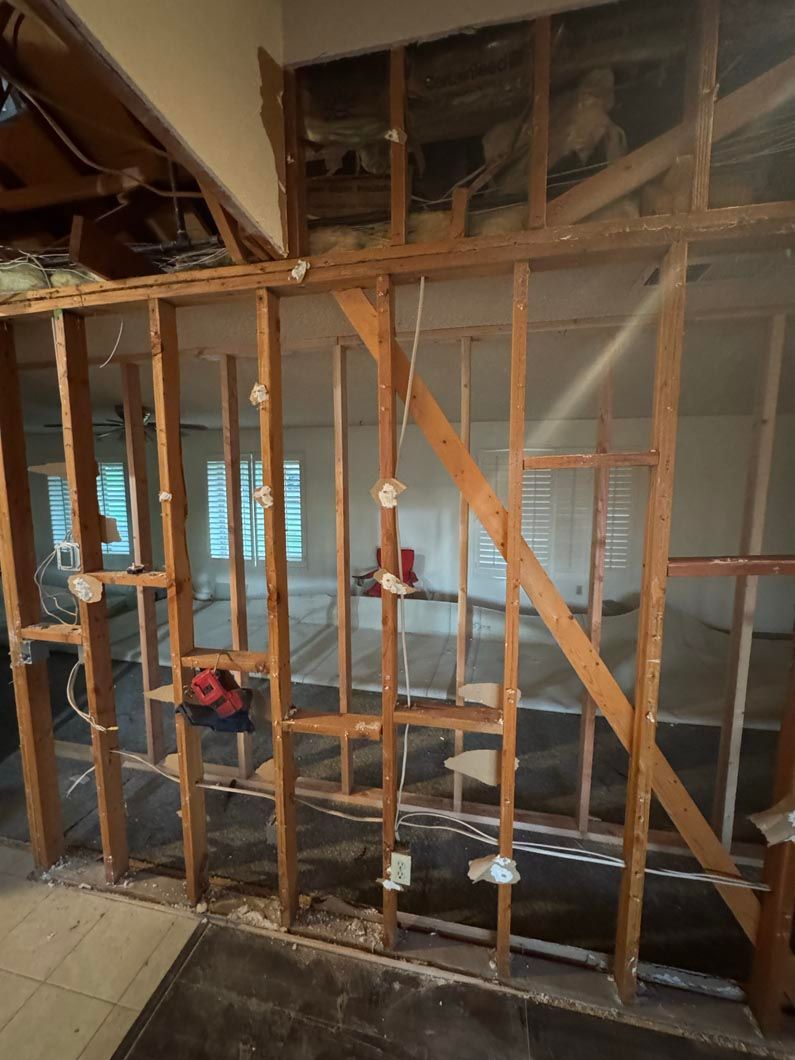 Exposed wooden framing inside a room, with tiled floor and windows visible through the studs.