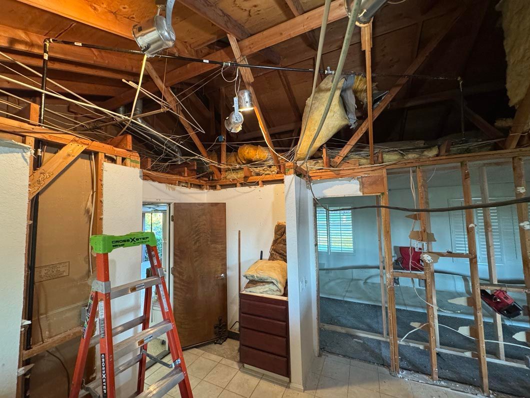 Partially demolished room with exposed ceiling beams, ladder, and wall framing under renovation