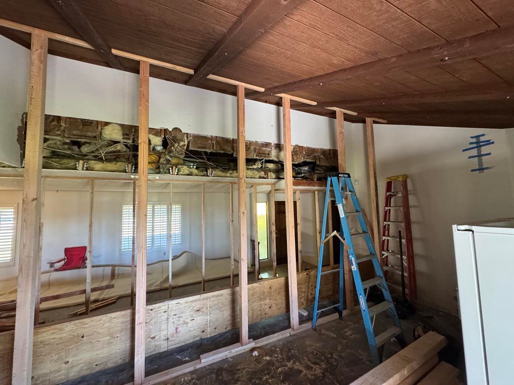 Interior under renovation with exposed wall studs, ladders, and insulation beneath a slanted ceiling